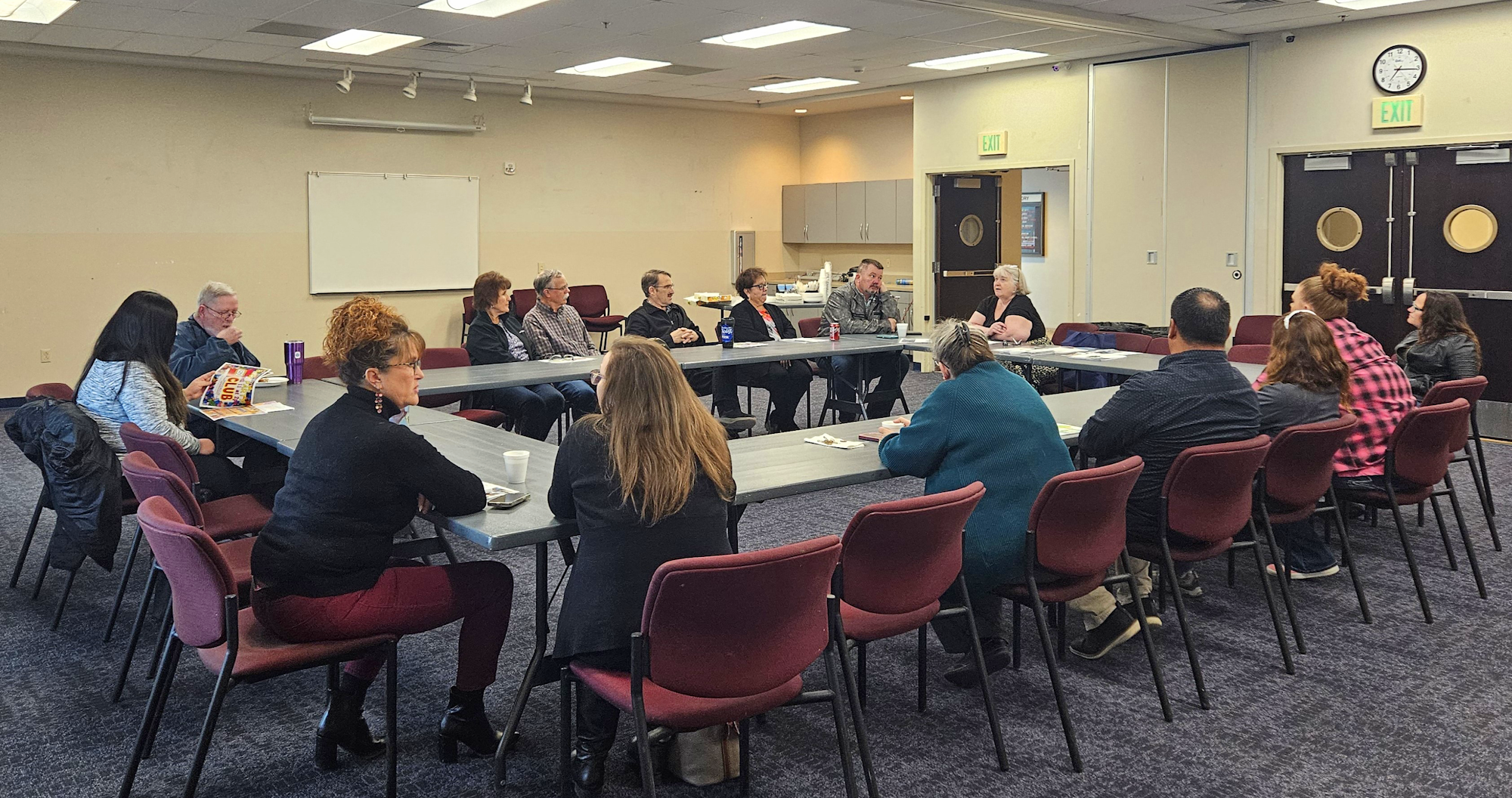 A group of people seated around a U-shaped table in a conference or meeting room.