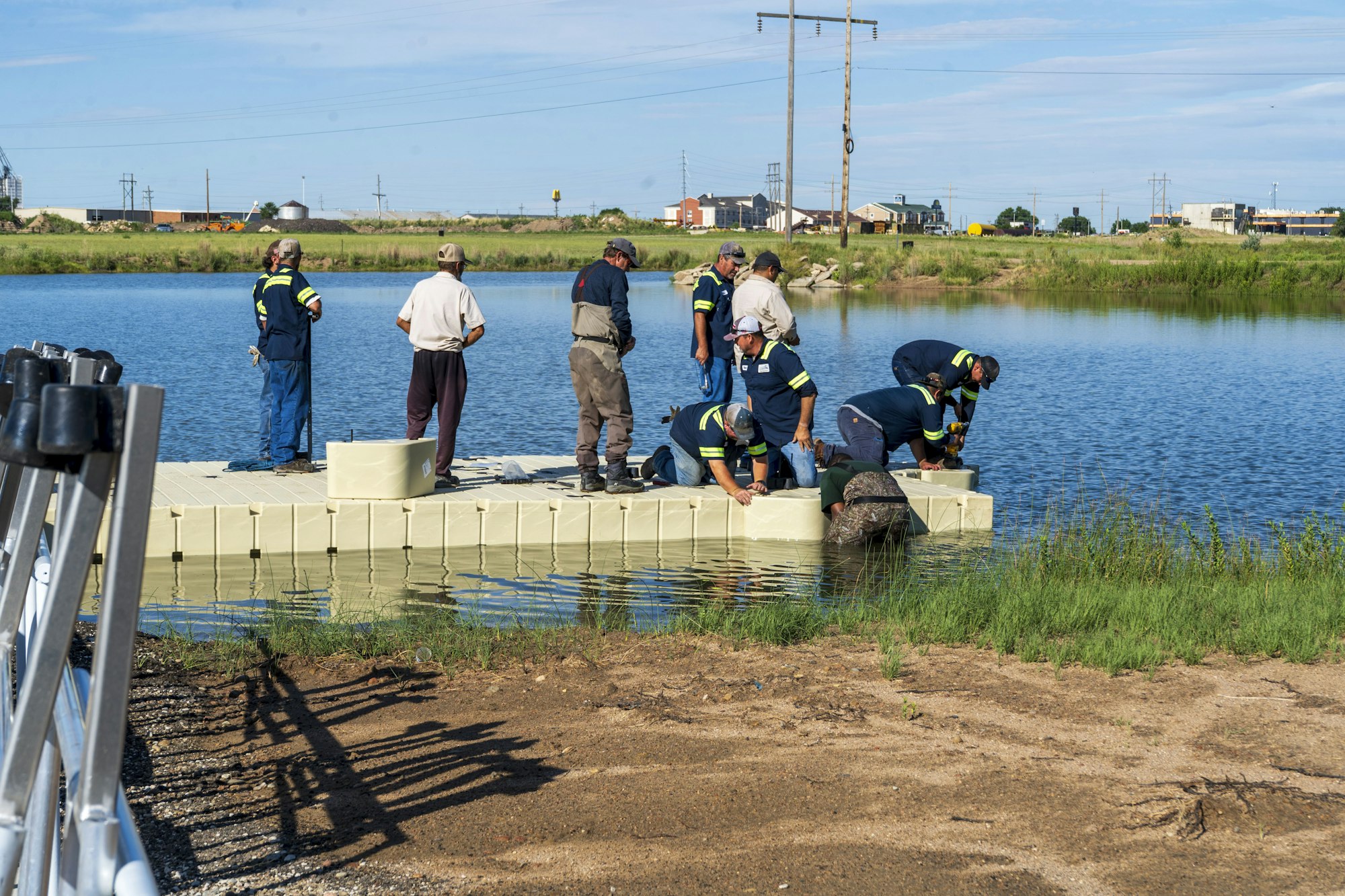 People assemble a floating platform on a lake under a clear sky.