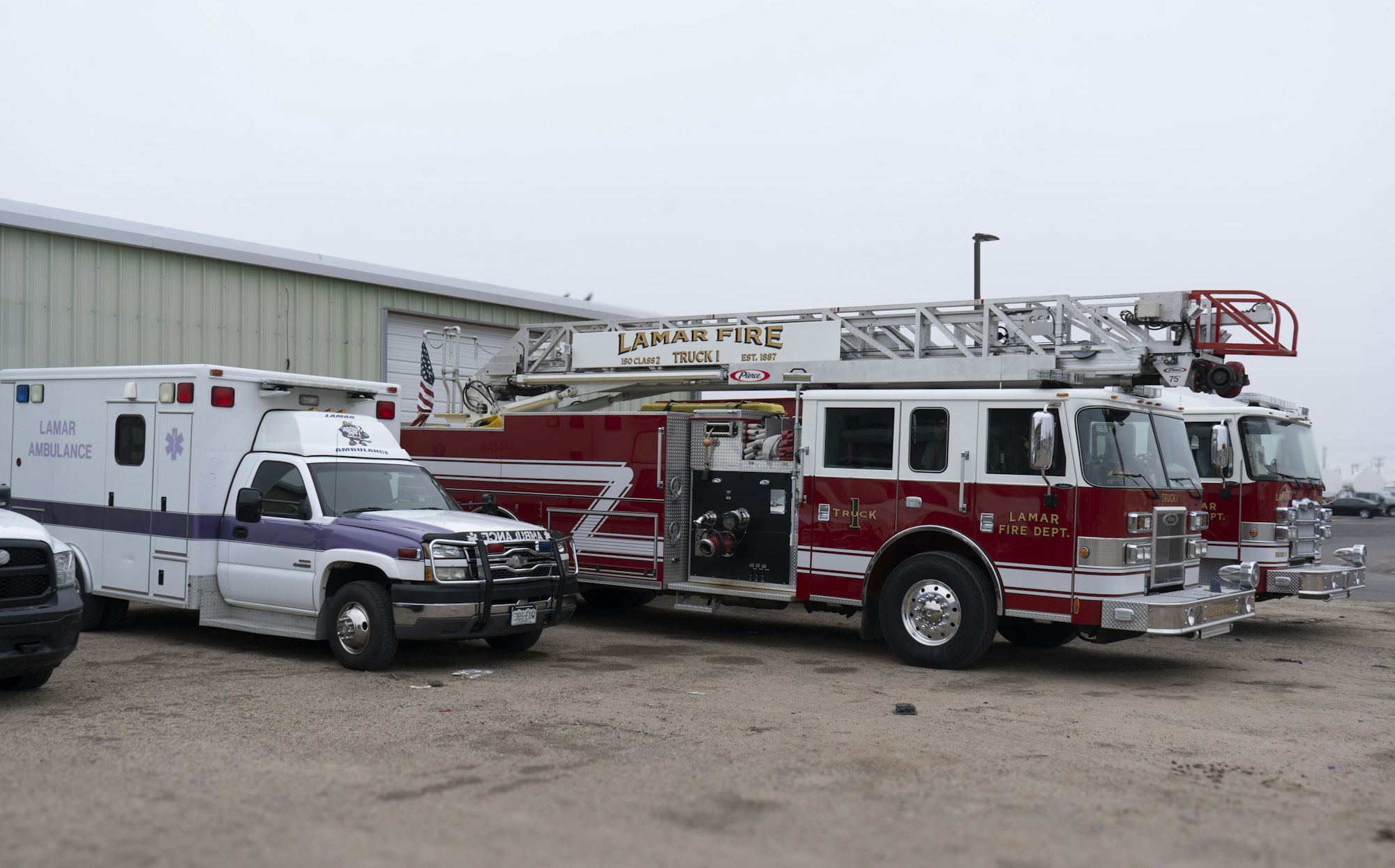 Ambulance and two fire trucks from Lamar Fire Dept. parked outside a building.