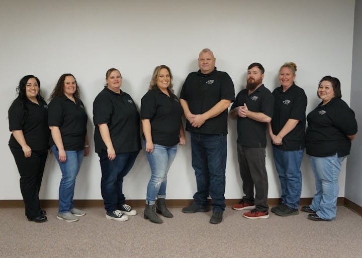 Eight Lamar Dispatch employees in a row, all wearing matching black shirts with logos, against a plain wall.