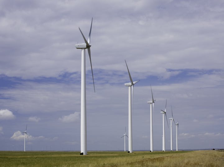 A row of wind turbines on a grassy field under a cloudy sky.