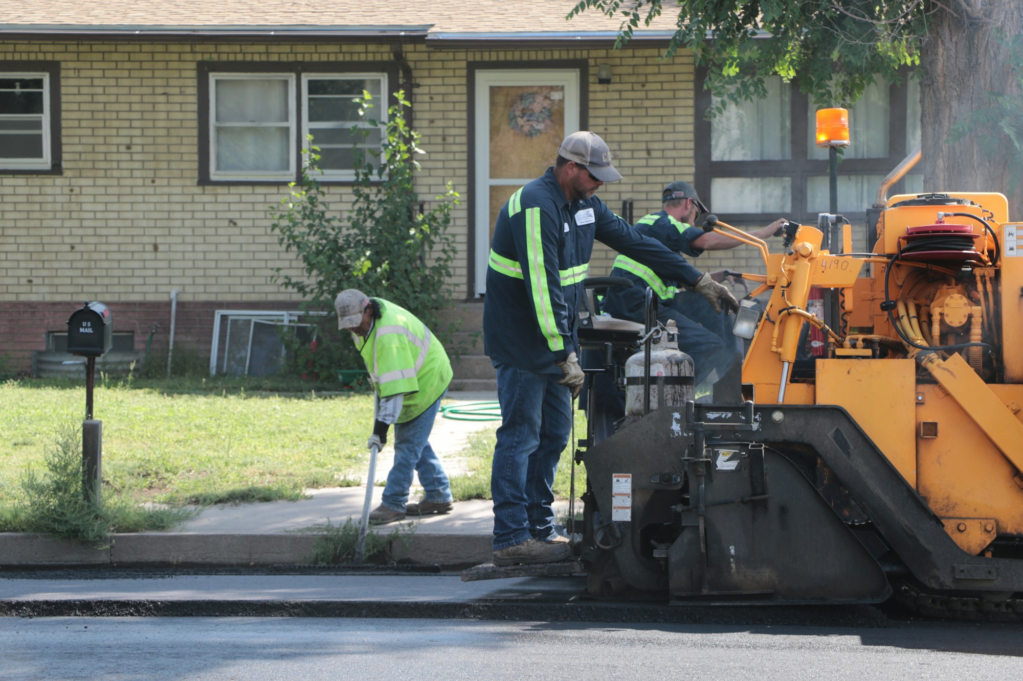 Workers in hi-vis gear operating machinery for road maintenance in front of a house.