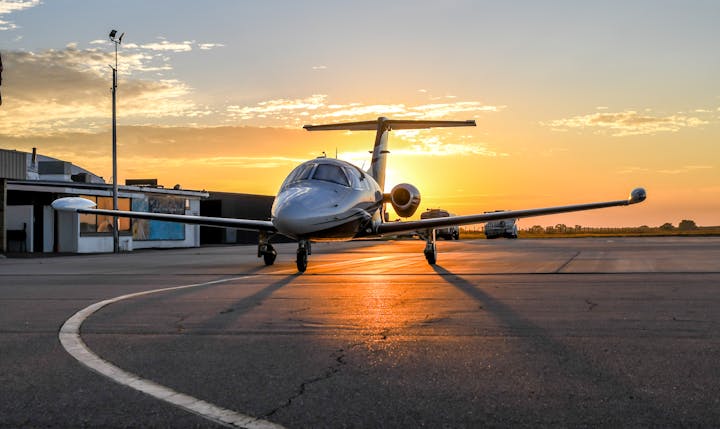 A small jet on a runway at sunset, with buildings and a fuel truck nearby.