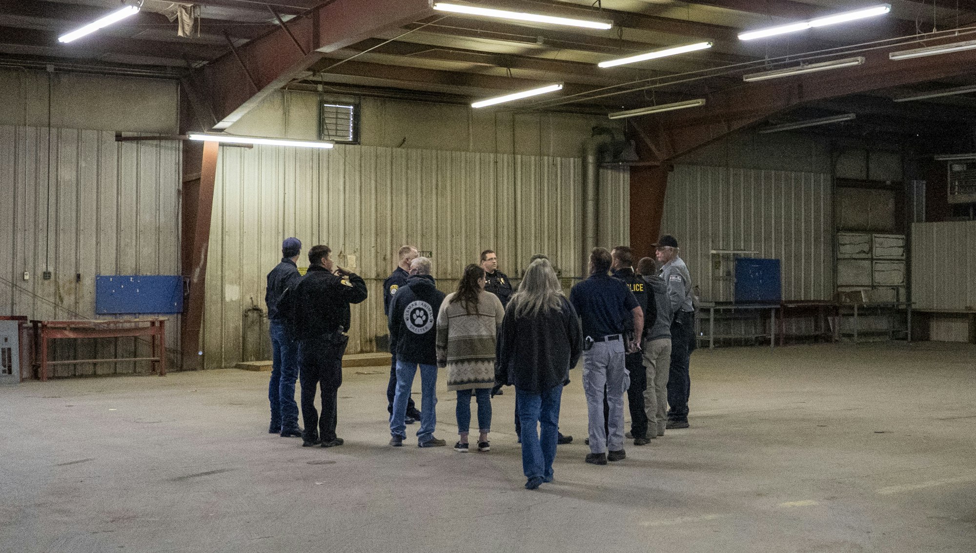 A group of people in casual and uniform clothing stand in a circle inside a large, industrial space.