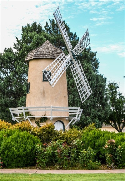 A traditional windmill surrounded by green shrubs under a blue sky.
