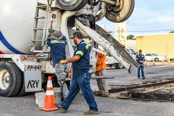 Workers operating a cement truck, pouring concrete at a construction site.