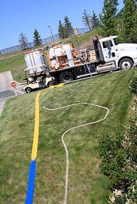 A truck with large tanks, hoses extending across a grassy slope, leading to something off-camera.
