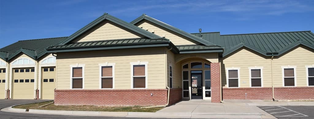 A beige building with a green roof, arched windows, and brick accents under a clear blue sky.