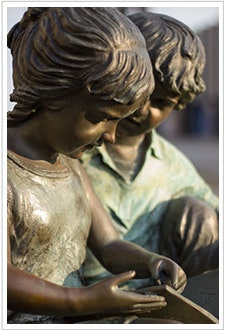 A close-up of a bronze sculpture depicting two children, a girl and a boy, focused on a shared activity.
