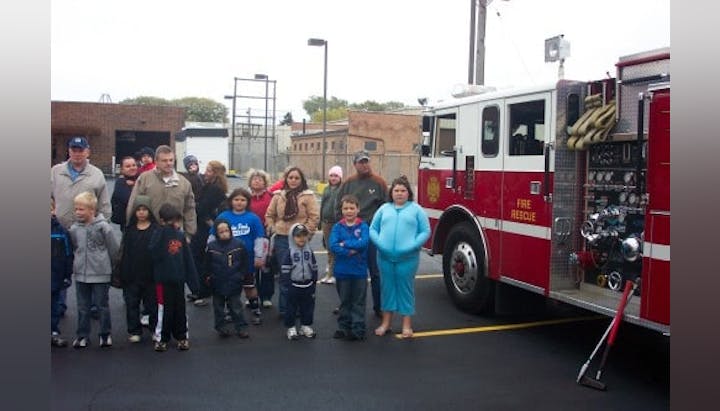 A group of people, including children, stand next to a fire truck parked on a street.