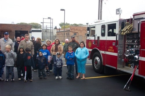A group of people, including children, stand next to a fire truck parked on a street.