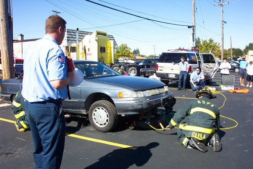 Firefighters in action at a car accident scene with people observing.