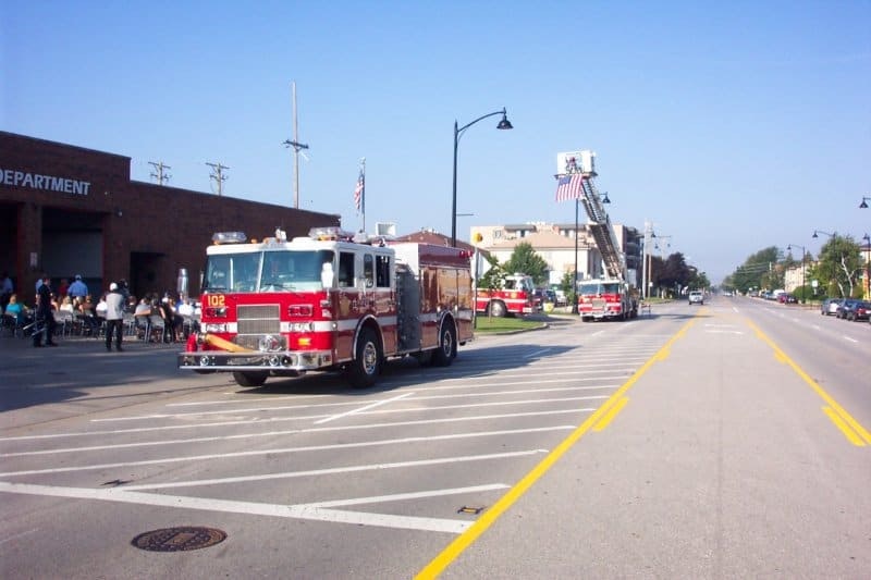 A fire truck is parked near a fire department, with people gathered outside. There are more fire trucks down the road.