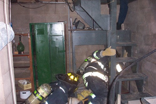 Firefighters in gear navigating a basement with metal stairs and storage lockers.