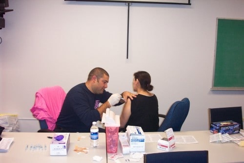 A person is receiving an injection in the arm from a healthcare professional in an office setting.