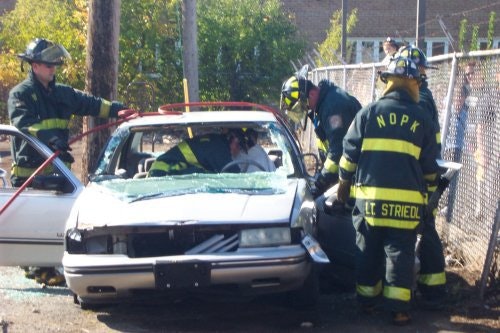 Firefighters are assisting in a car accident scene, working on a damaged car with a person inside.