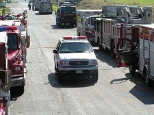 Emergency vehicles with flashing lights are on a road, including fire trucks and a white SUV.