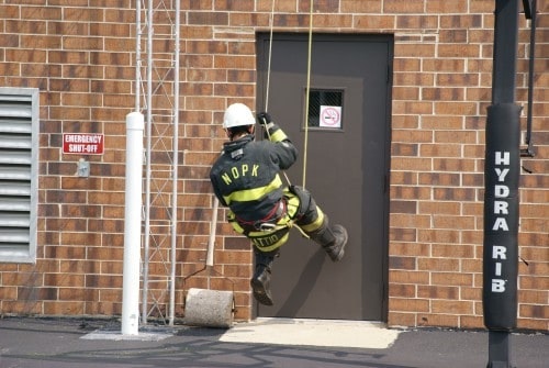 A firefighter rappelling down a building wall near a door marked "Hydra Rib."