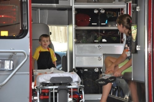 Two children sitting inside an ambulance, one on a stretcher, the other on a ledge, surrounded by medical equipment.