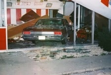 A car crashed into a building, smashing the glass front and causing debris inside.