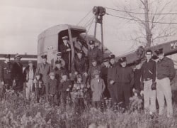 A group of people, including children, gathered around a vintage vehicle in a field, possibly for a photograph or event.