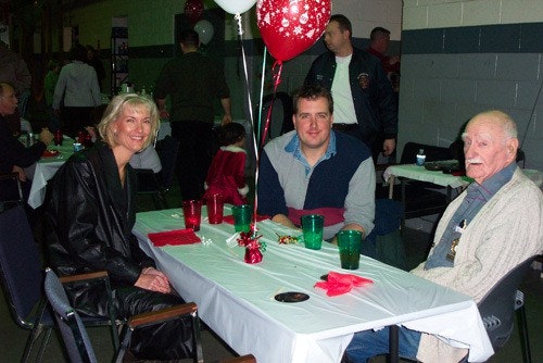 Three people sitting at a table with red balloons and drinks, in a festive setting.