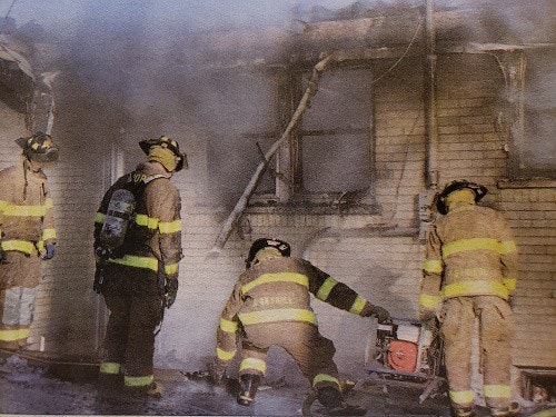 Four firefighters in gear, managing a smoky fire in a building.