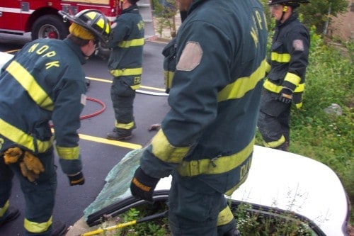 Firefighters in action at a scene involving a vehicle, with protective gear and equipment visible.