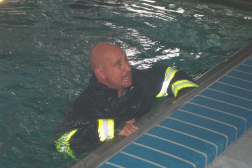 A person in a pool wearing a wet suit with reflective stripes, holding onto the pool edge.