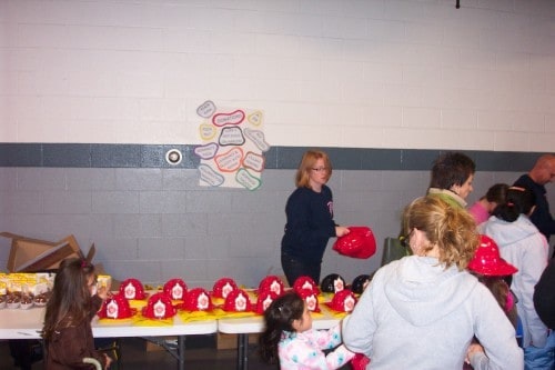 People gathered around a table with red firefighter helmets and snacks in a room with a poster on the wall.