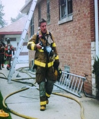 A firefighter in gear walks away from a building with hoses and ladders after an operation.