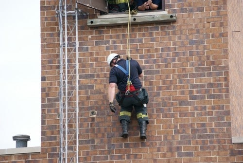 A person in safety gear is rappelling down a brick building.