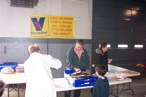 People at a distribution event, with a Vienna Beef sign and a mention of delivery services in Chicago.