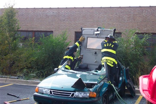 Firefighters removing the roof of a green car with tools, possibly during a rescue operation.