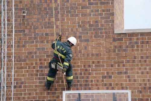 A person in safety gear rappelling down a brick building using a rope.