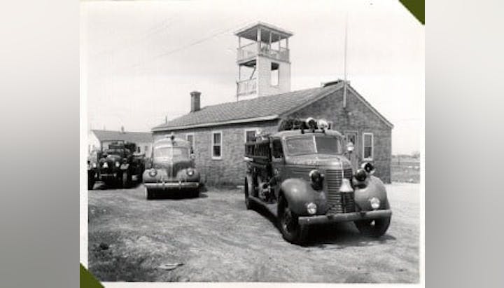 Vintage fire station with classic cars and a fire truck parked outside. Station under construction.
