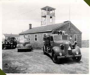 Vintage fire station with classic cars and a fire truck parked outside. Station under construction.