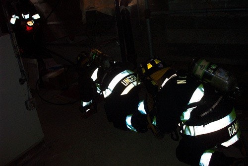 Firefighters in reflective gear crouching inside a dimly lit building.
