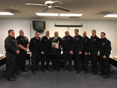 A group of firefighters in uniform stand together in a room, with one holding a certificate or plaque.