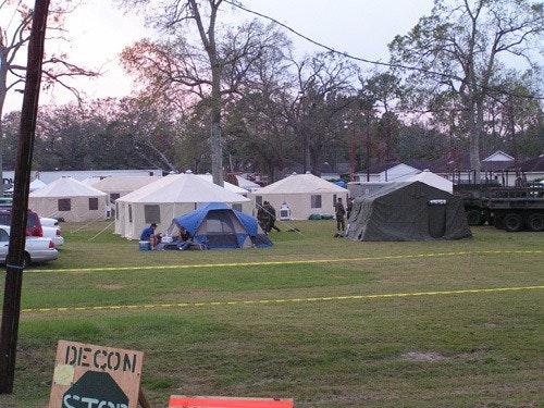 An outdoor camp with multiple tents, people, a truck, and a "DECON" sign on the grass.
