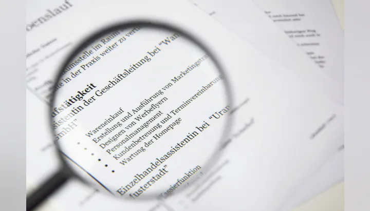 The image shows a document, possibly a resume, with text about job responsibilities highlighted through a magnifying glass.