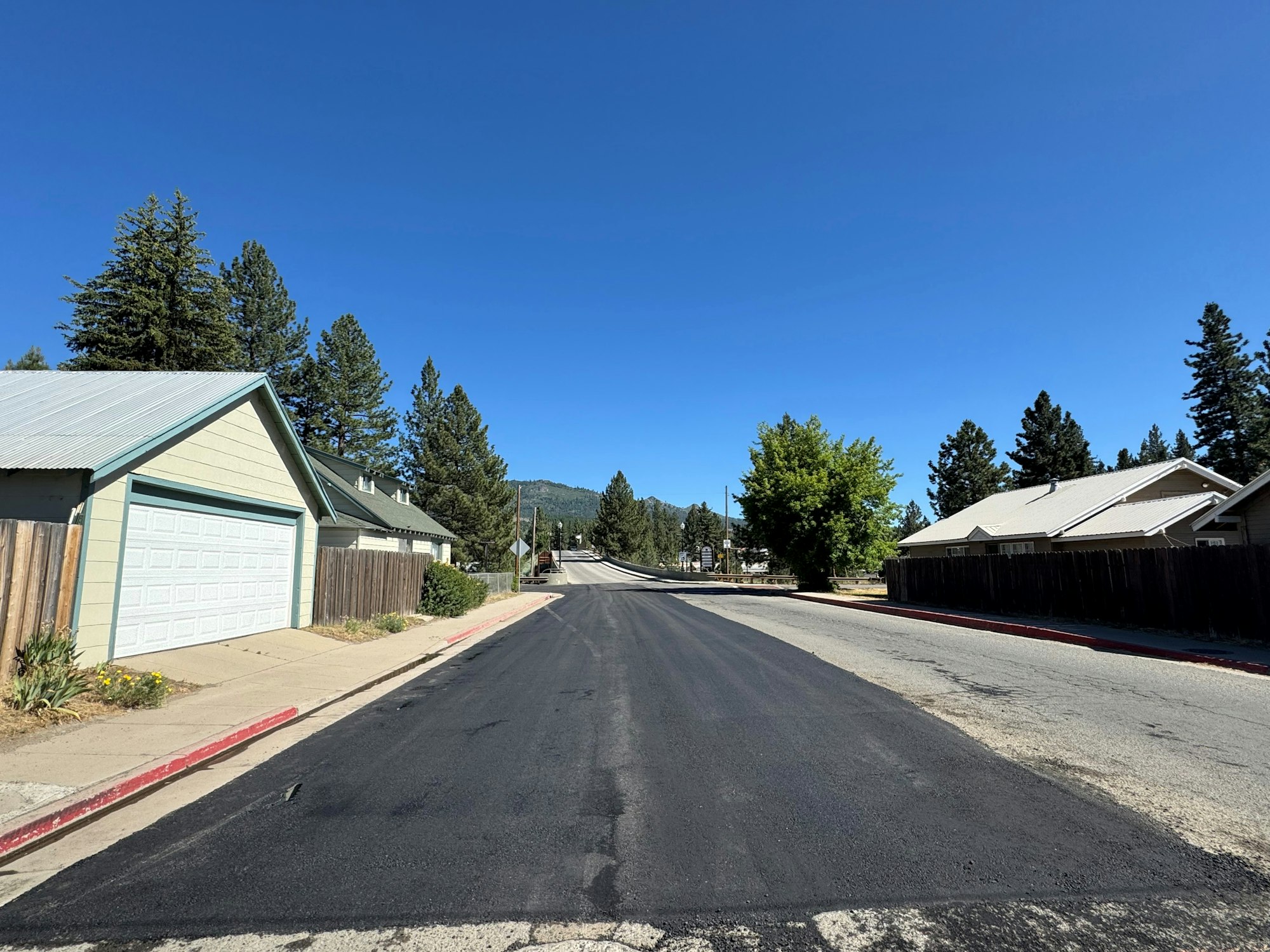 A quiet suburban street with houses, trees, and clear blue sky.