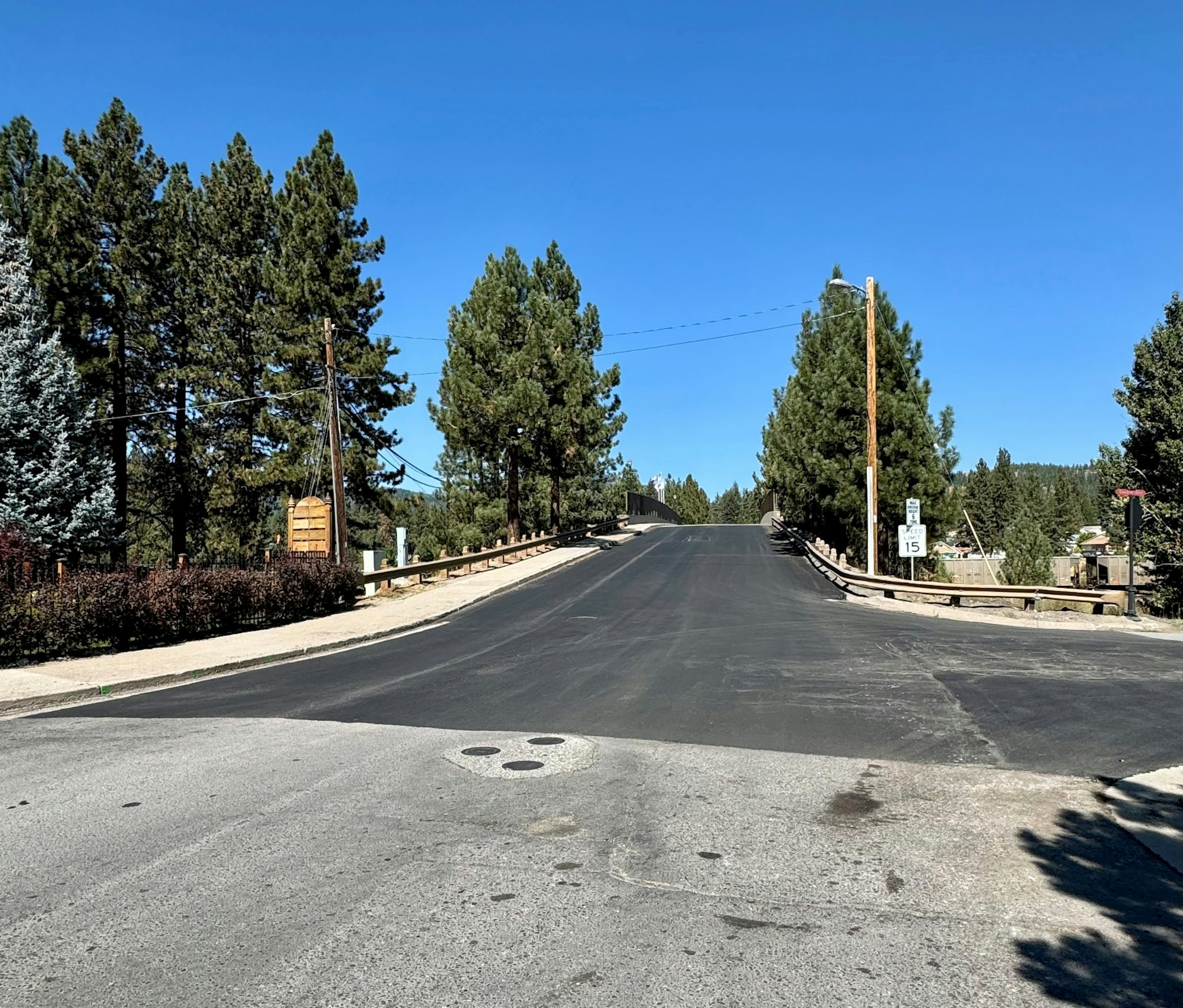 A paved road surrounded by trees and a 15 mph speed limit sign under a clear blue sky.