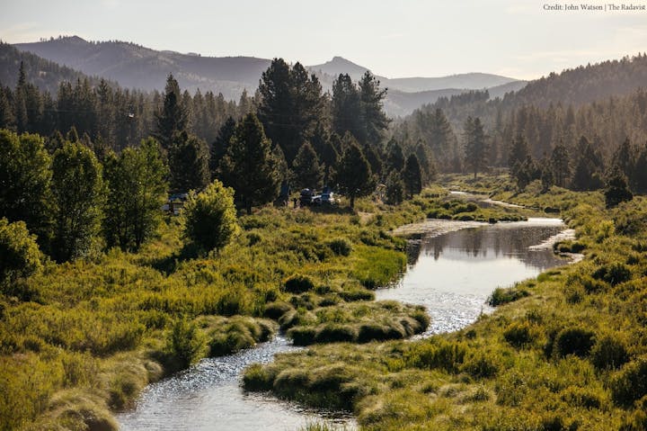 A serene landscape with a winding river, lush greenery, and distant mountains under a clear sky.