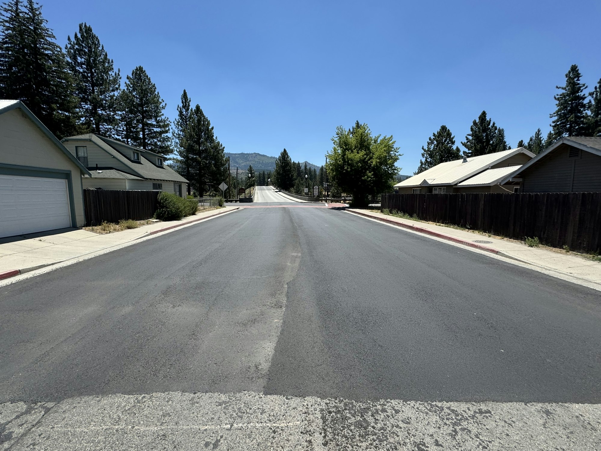 A wide, empty street lined with houses and trees under a clear blue sky.