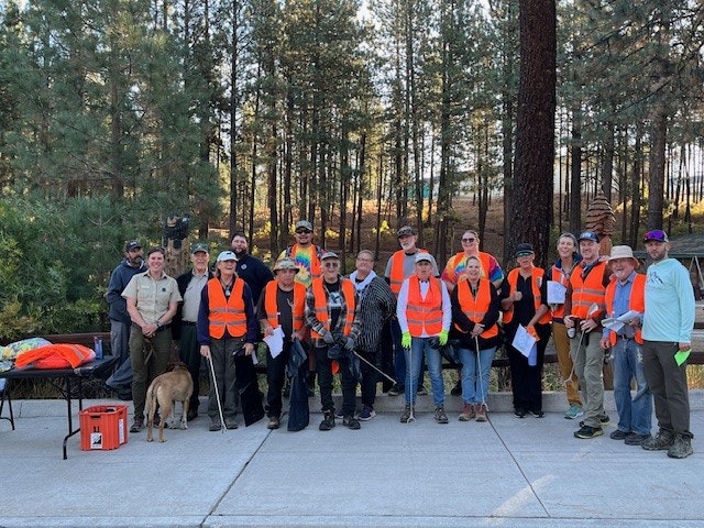 A group of people in orange safety vests standing outdoors with trees in the background.