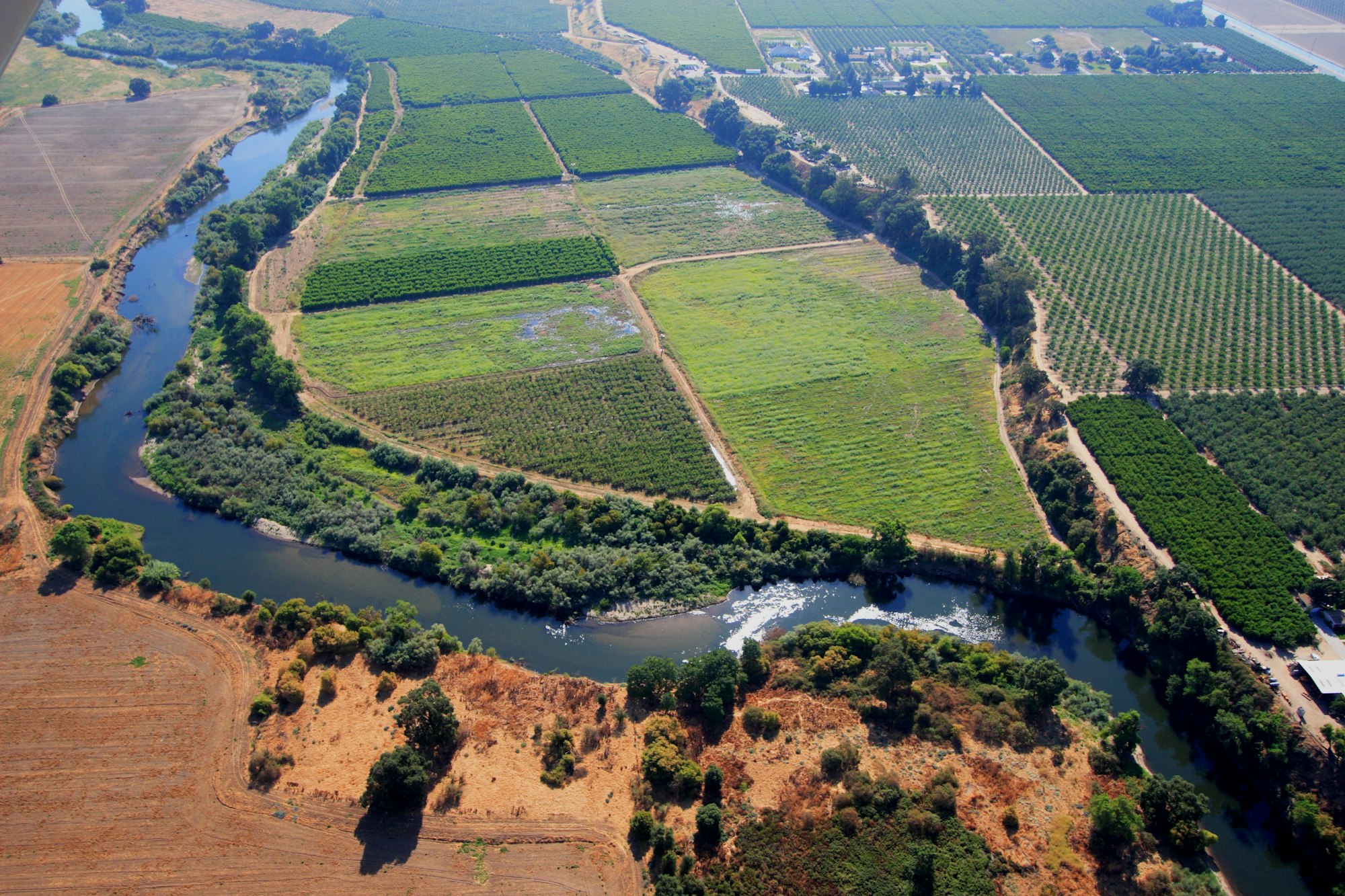 Aerial view of lush farmland with a winding river and fields, showcasing a mix of crops and green vegetation.