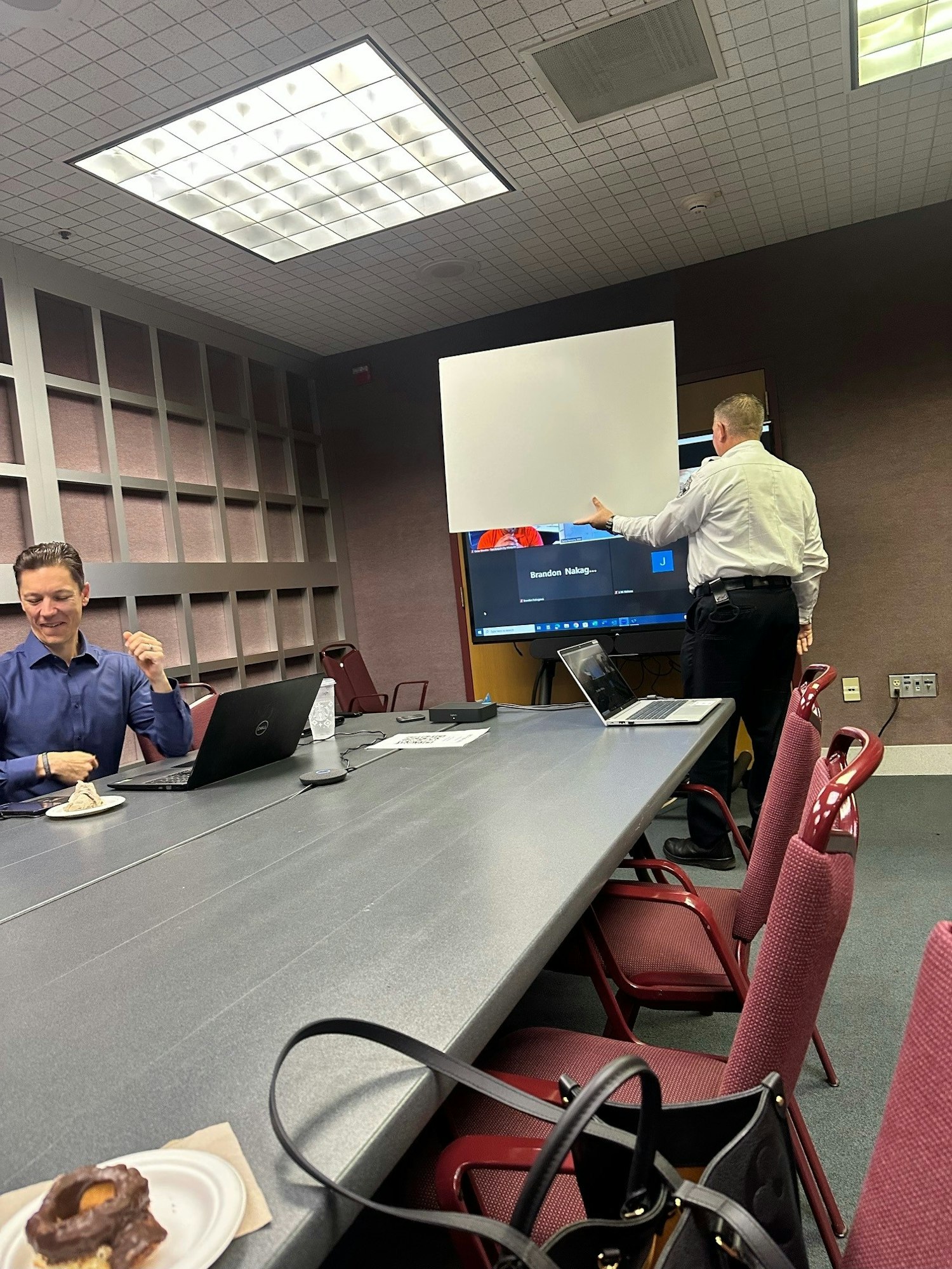 May contain: adult, male, man, person, indoors, clothing, footwear, shoe, people, computer, electronics, laptop, pc, crowd, accessories, bag, handbag, furniture, table, and plate