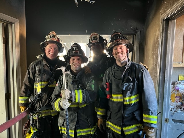 Firefighters posing together in a burned room, showcasing camaraderie and resilience after a fire response.