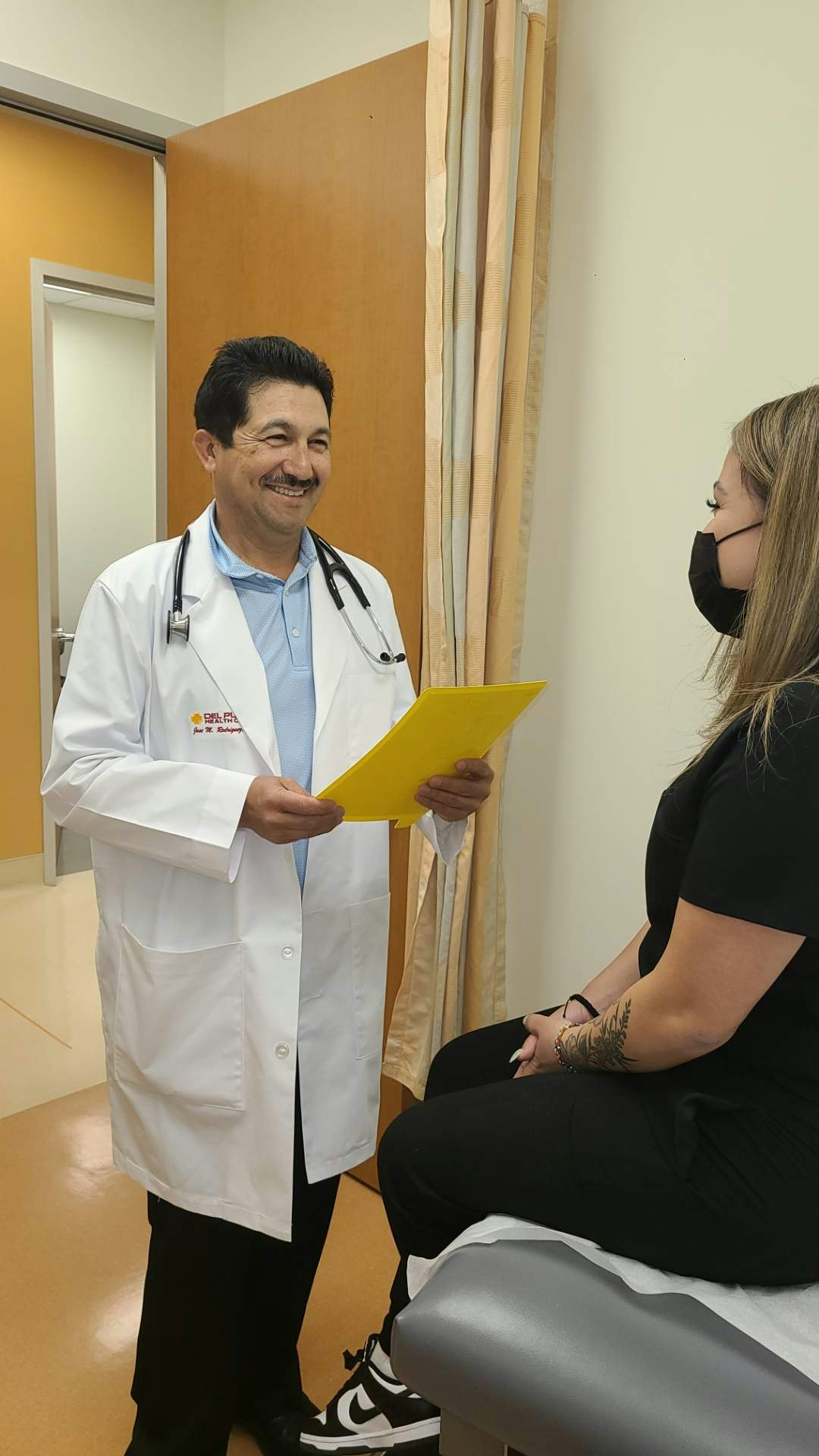 A doctor in a white coat is consulting with a patient sitting on an exam table, both are smiling and engaged in conversation.